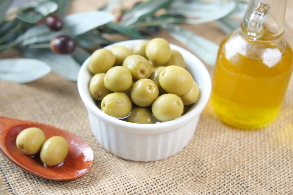 Close-up of fresh green olives in a bowl with a bottle of olive oil on a textured surface.