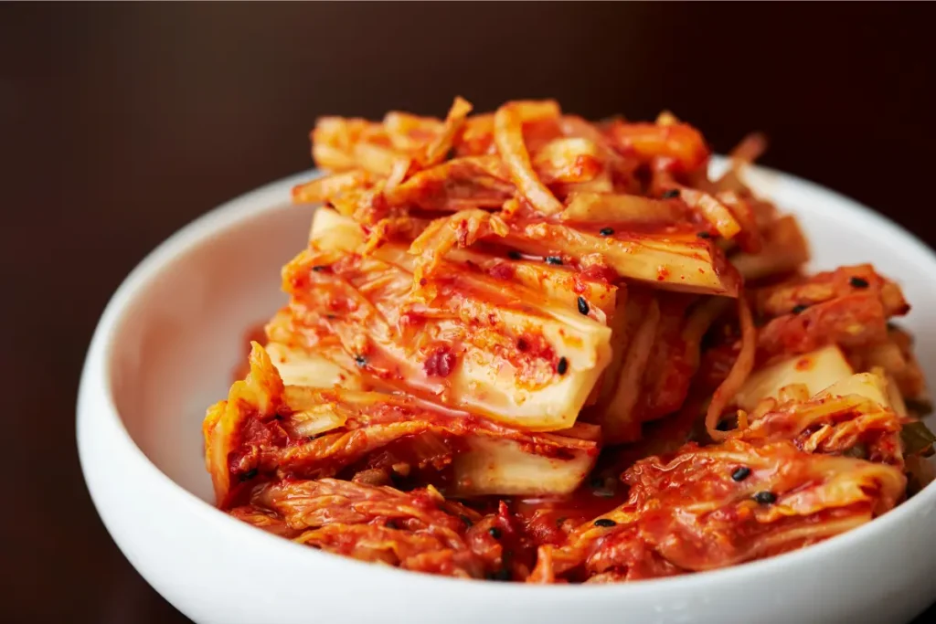 Satu mangkuk penuh kimchi merah merona dengan taburan wijen dan irisan daun bawang segar di atas meja makan.