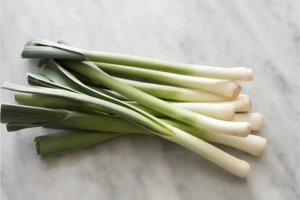 Kumpulan batang daun bawang murni yang segar dengan akar putih bersih diletakkan mendatar di atas meja dapur.